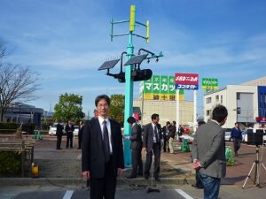 上部の風車のブレードがマグネシウム合金製。手前は技術開発・試験評価に携わった青柳教授。